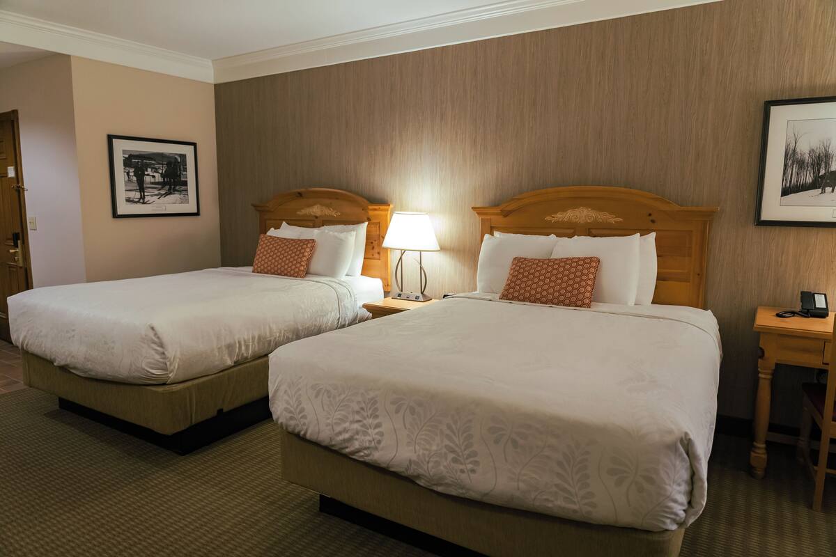 Une chambre d’hôtel avec deux lits, chacun doté d’une tête de lit en bois, d’une table de chevet avec une lampe et d’un tableau encadré au mur.