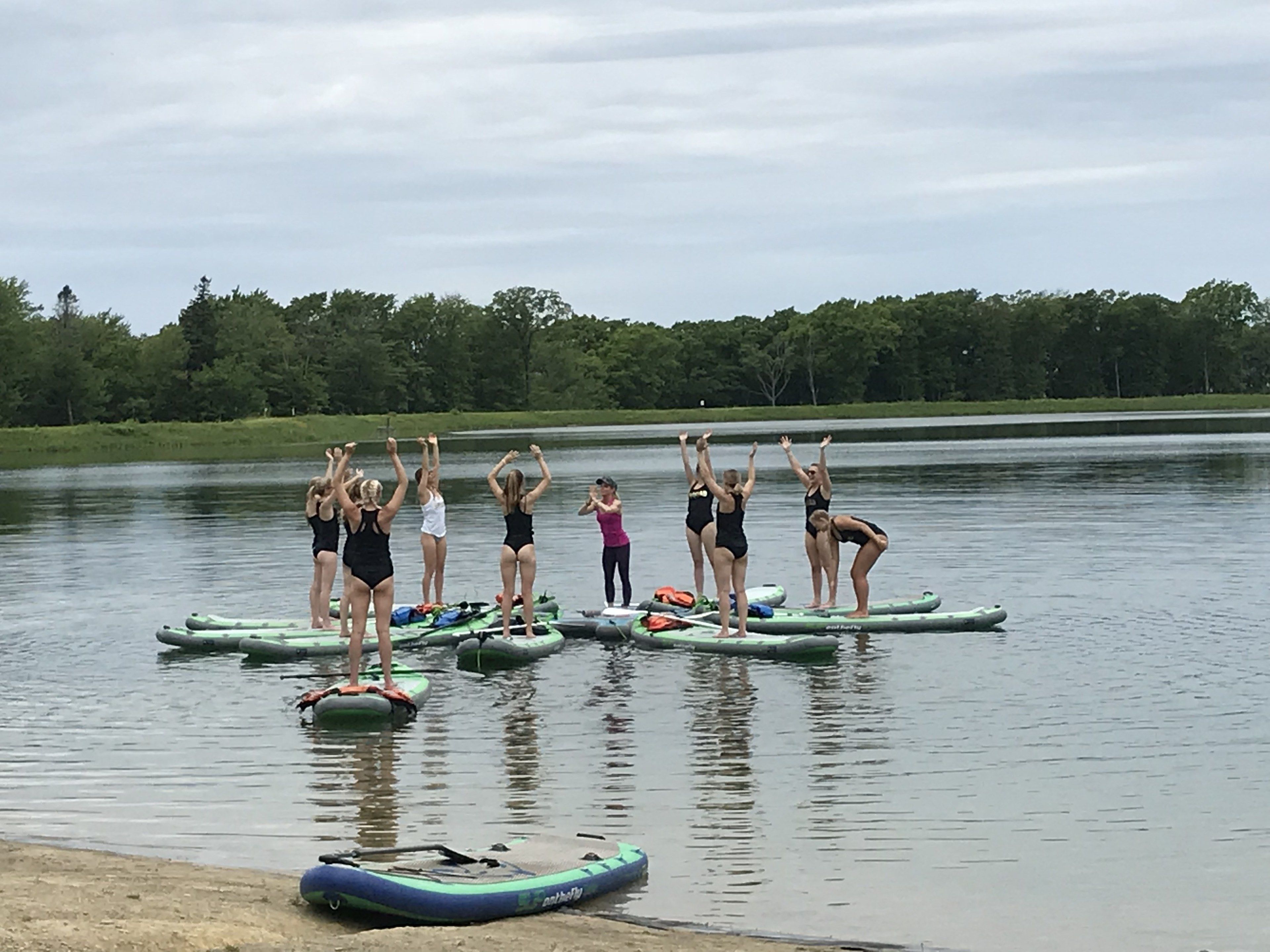 A group of people on paddleboards in a calm lake with trees in the background.