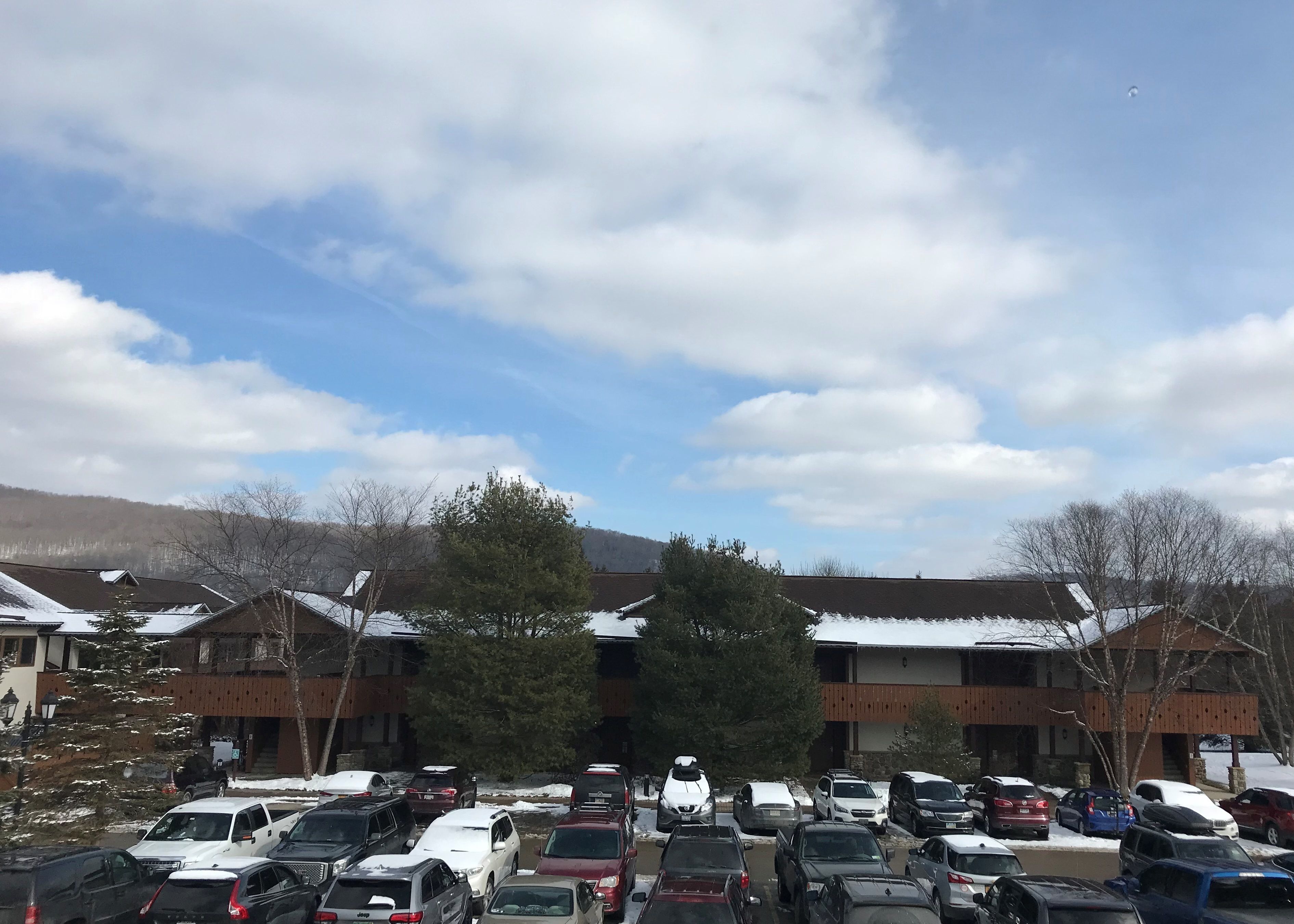 A parking lot with multiple cars and a building with a sloped roof in the background.