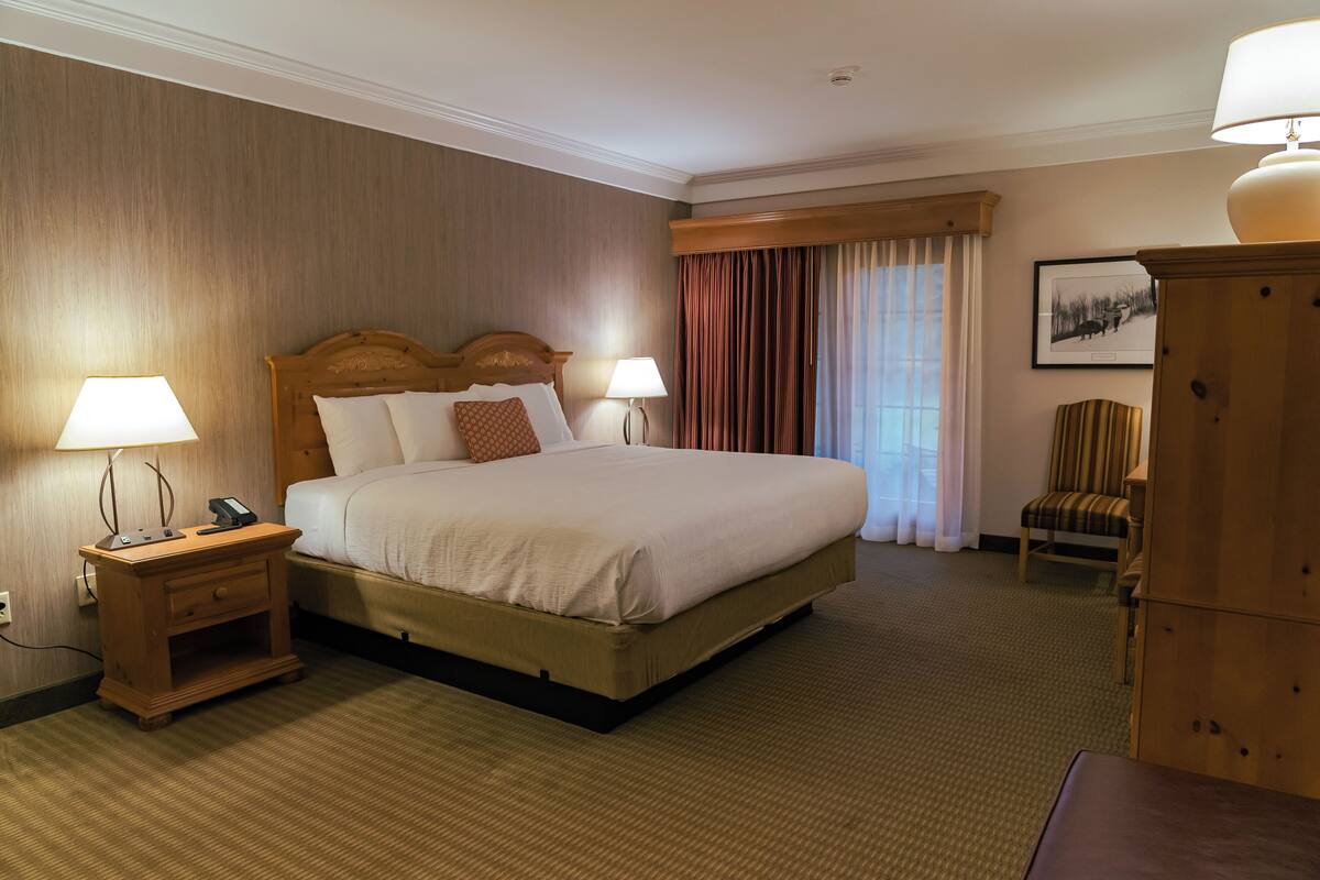 Une chambre d’hôtel avec un grand lit, deux tables de chevet avec des lampes, une chaise et une armoire en bois.