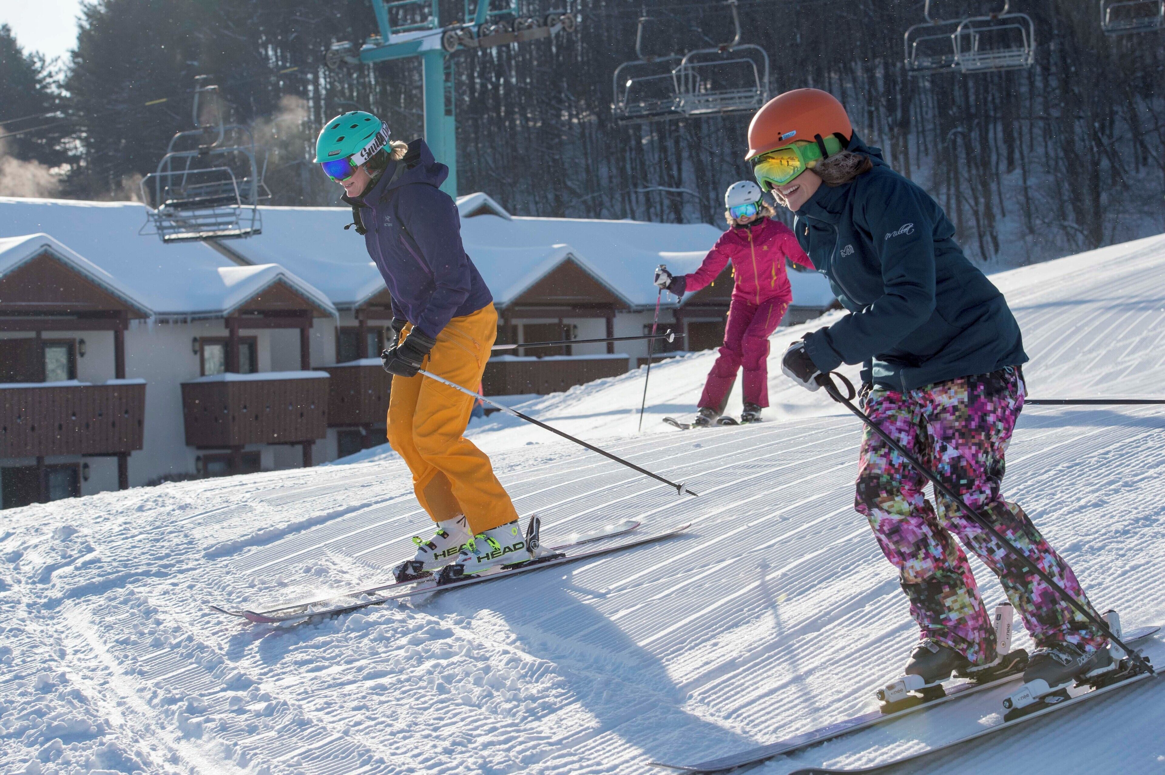 A ski slope with skiers, a ski lift, and buildings in the background.