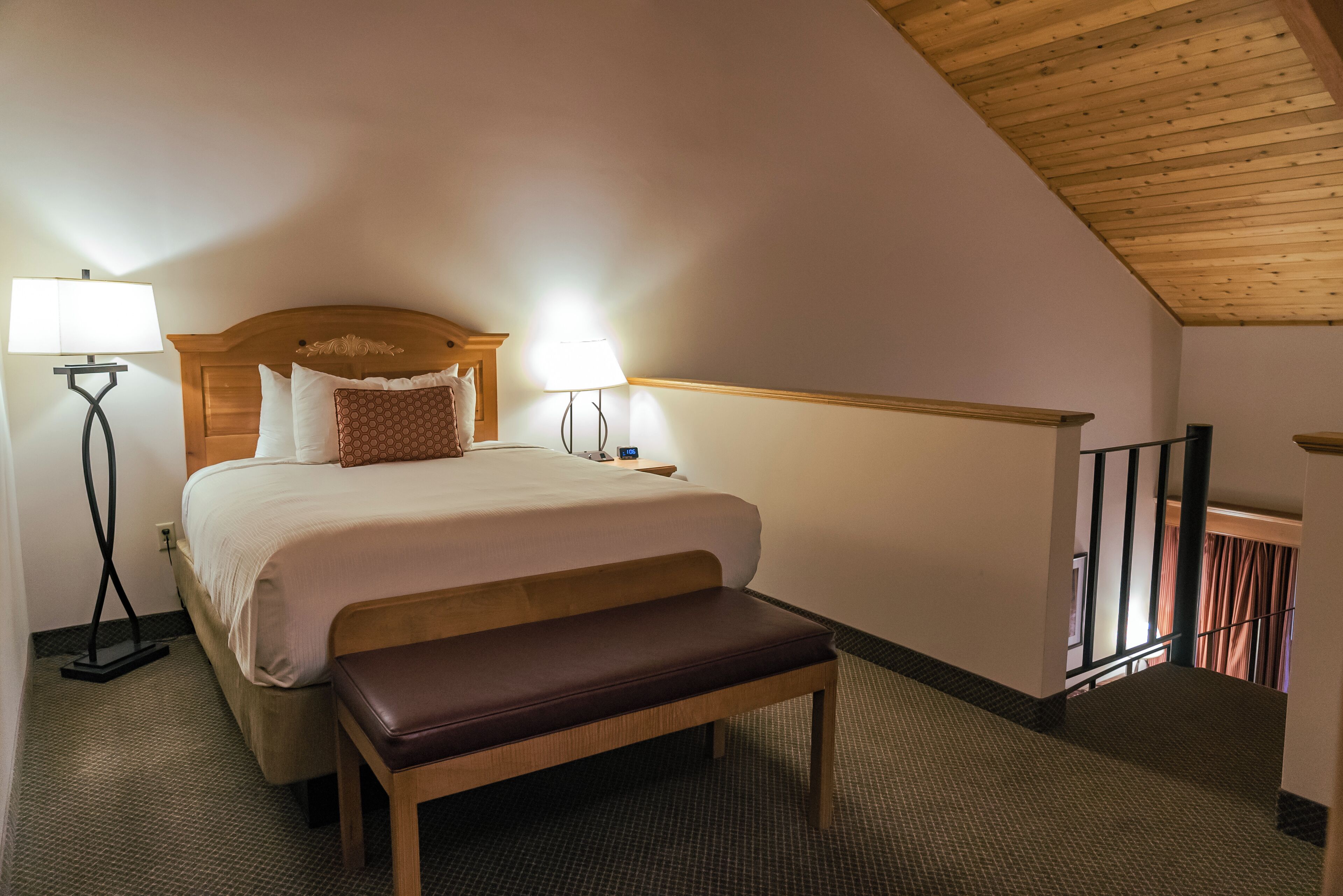 Une chambre à coucher avec un lit, deux lampes de chevet, un banc et un plafond en bois.