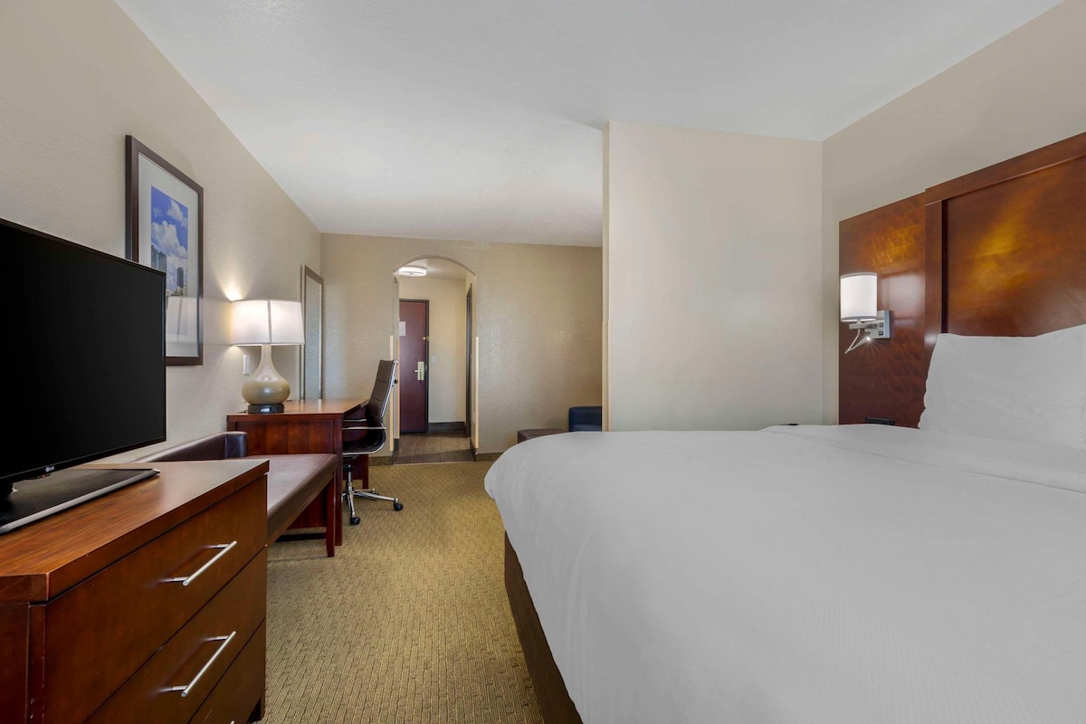 Habitación de hotel con cama, escritorio con televisor, silla, lámpara y puerta que da a otra habitación.