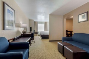 Una habitación de hotel con cama, un escritorio con lámpara, un sofá azul y un televisor.