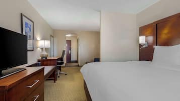 Habitación de hotel con cama, escritorio con computadora, televisión, lámpara y puerta que da a otra habitación.