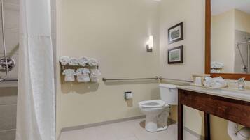 A bathroom with a toilet, sink, and shower. There are towels and a hand dryer on the wall.