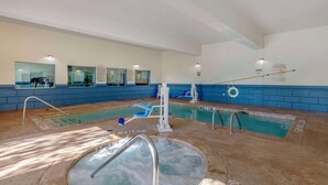 Una piscina interna con idromassaggio, pareti piastrellate di blu e una postazione per il bagnino.