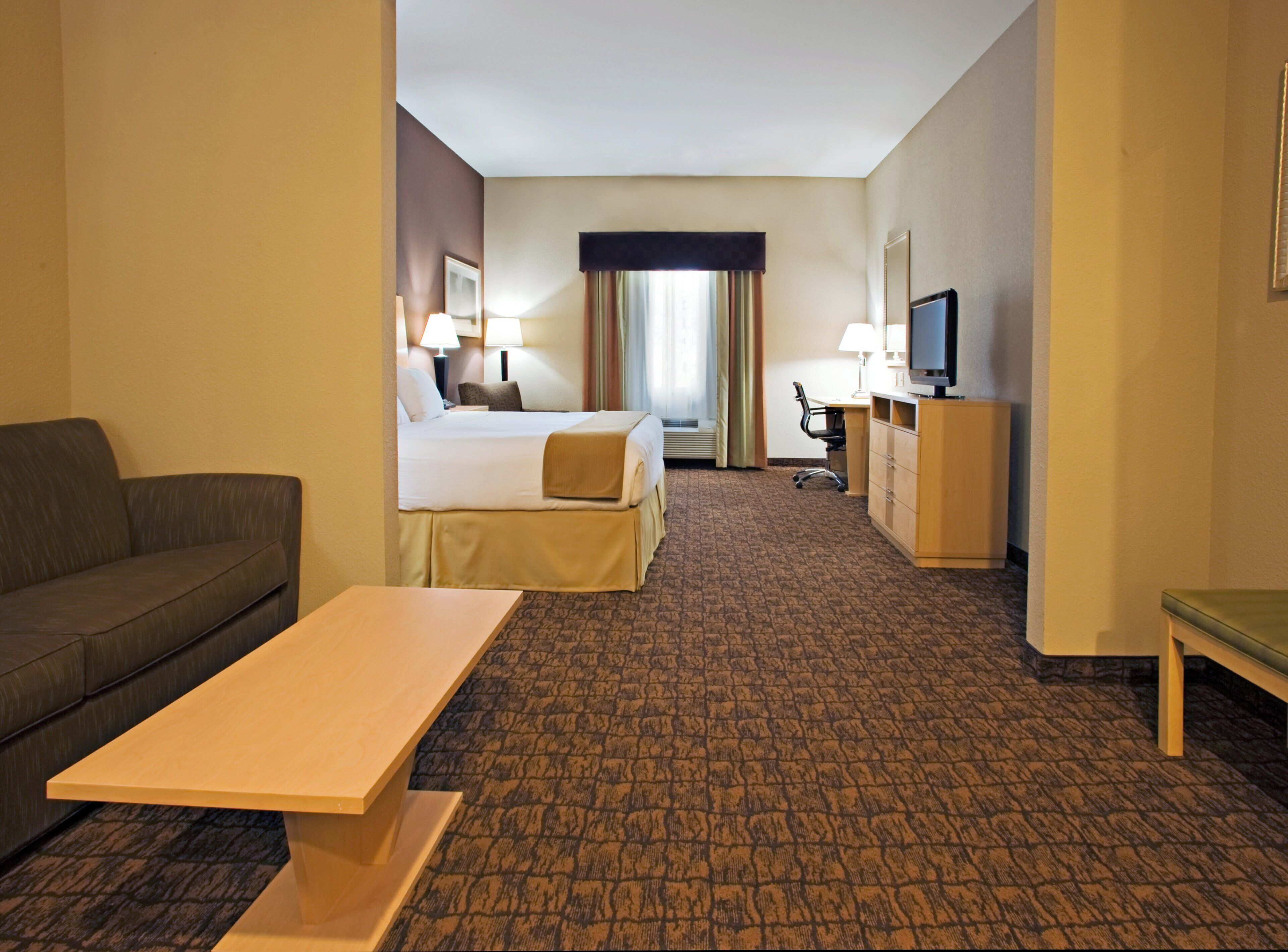 A hotel room with a bed, a desk, a chair, a television, and a sofa.