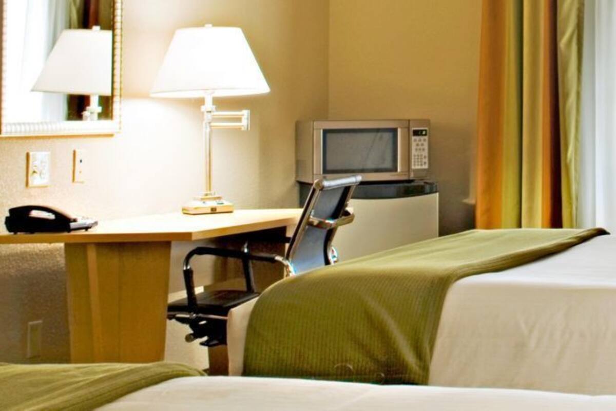 A hotel room with two beds, a desk with a computer and a phone, a TV, and a window with curtains.