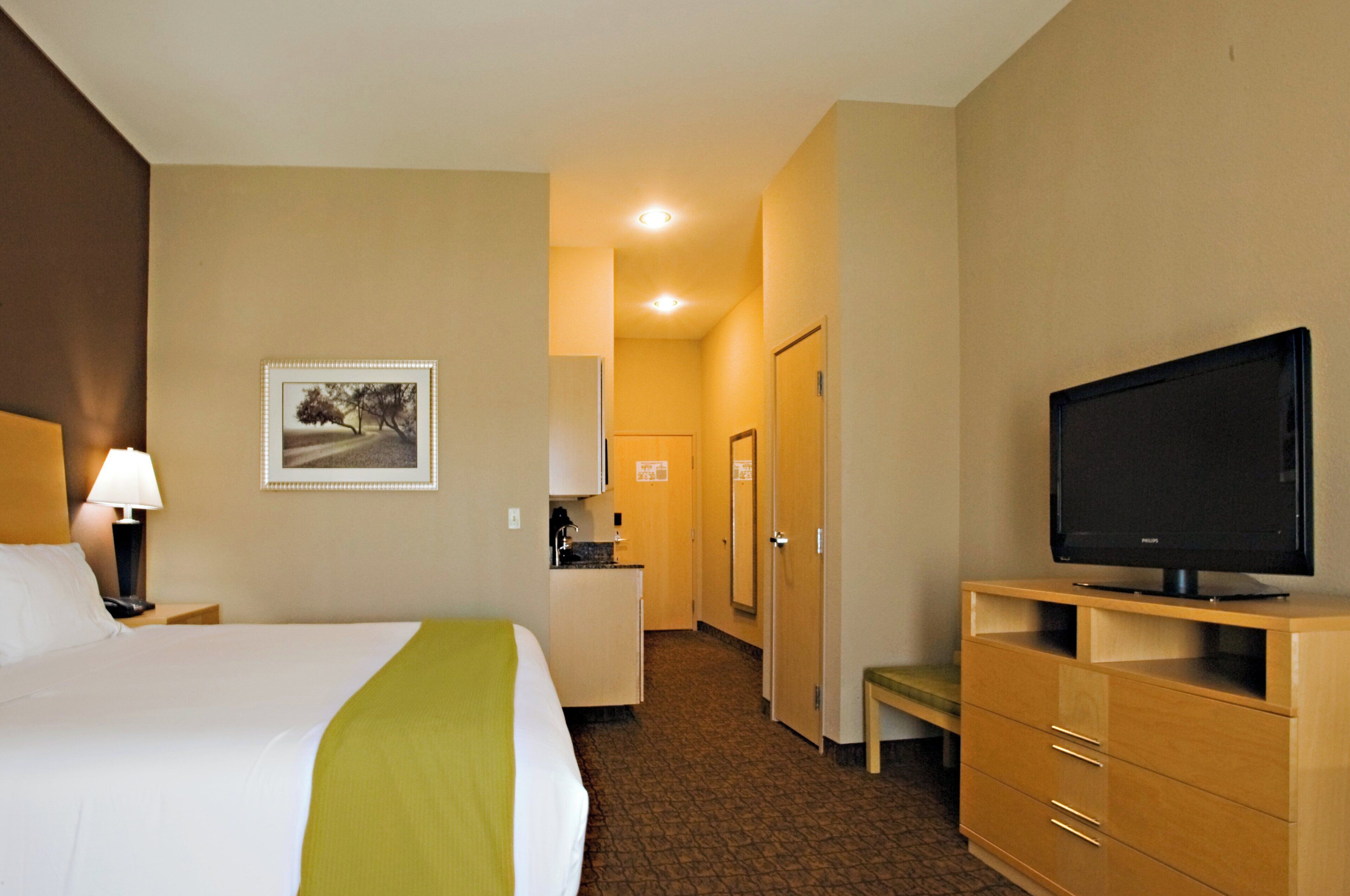 A hotel room with a bed, a television, a desk with a lamp, and a picture on the wall.