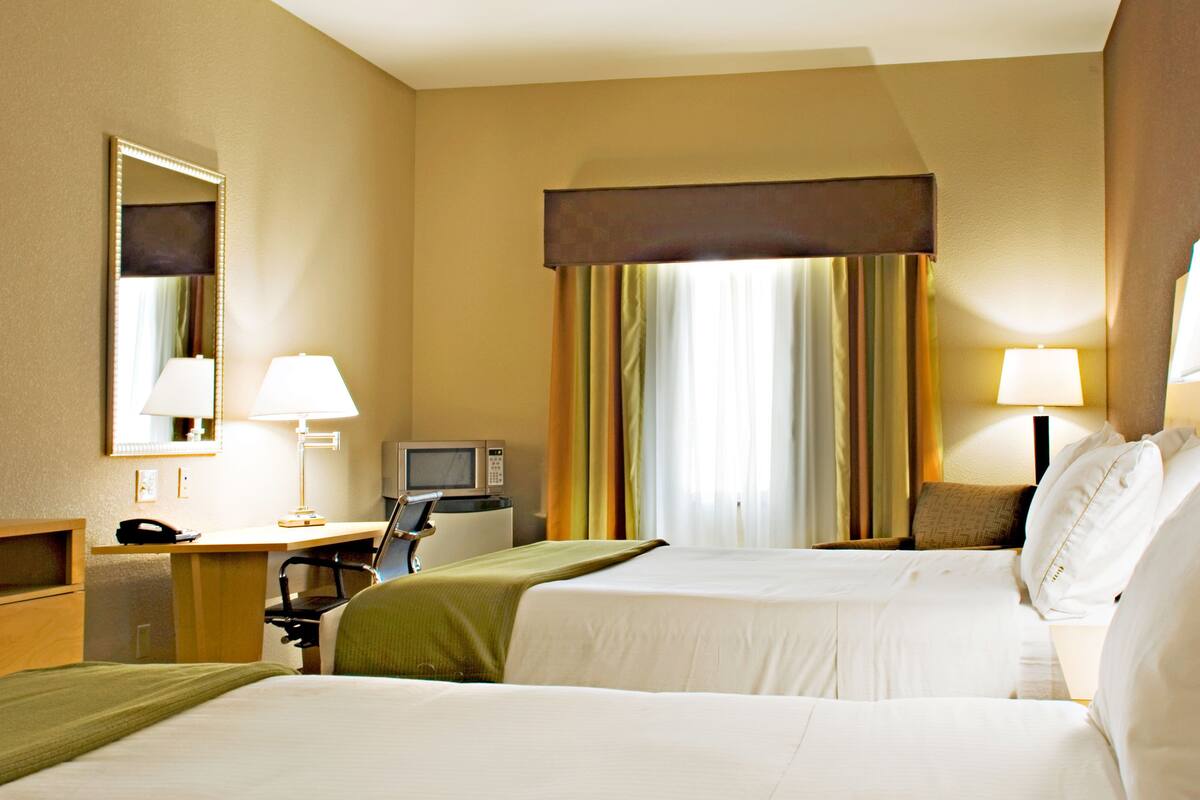 A hotel room with two beds, a desk with a lamp, a telephone, a television, and a window with curtains.