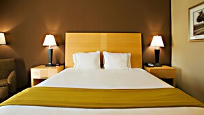 A hotel room with a large bed, two bedside tables with lamps, a chair, and a framed picture on the wall.