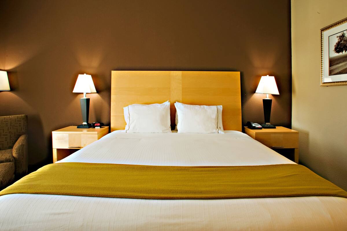 A hotel room with a large bed, two bedside tables with lamps, a chair, and a framed picture on the wall.