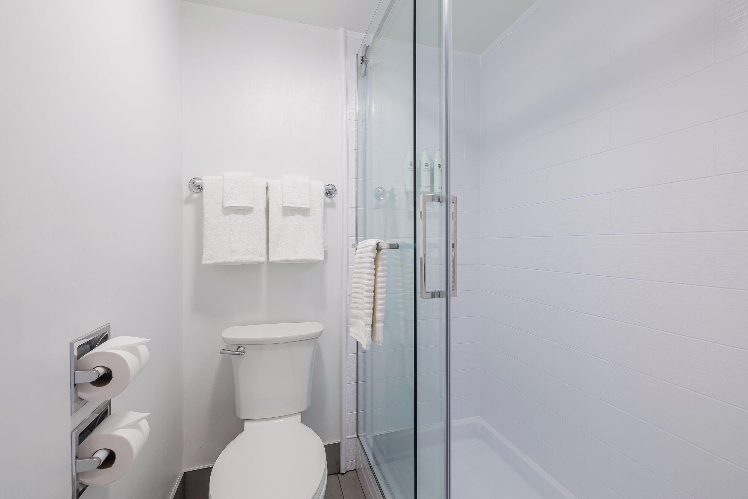 A modern bathroom with a glass-enclosed shower, a toilet, and a towel rack with two towels.