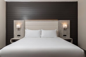 A hotel room with a large bed, two bedside tables, and wall-mounted lamps. - Oakfield Hotel & Suites, Ascend Collection, Rochester-Pittsford NY (Rochester)