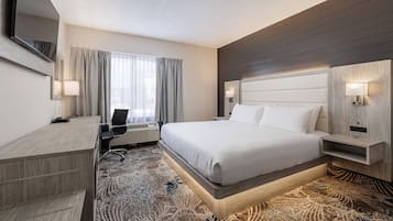Une chambre d’hôtel avec un grand lit, un bureau, une chaise, un téléviseur à écran plat et une fenêtre avec des rideaux.