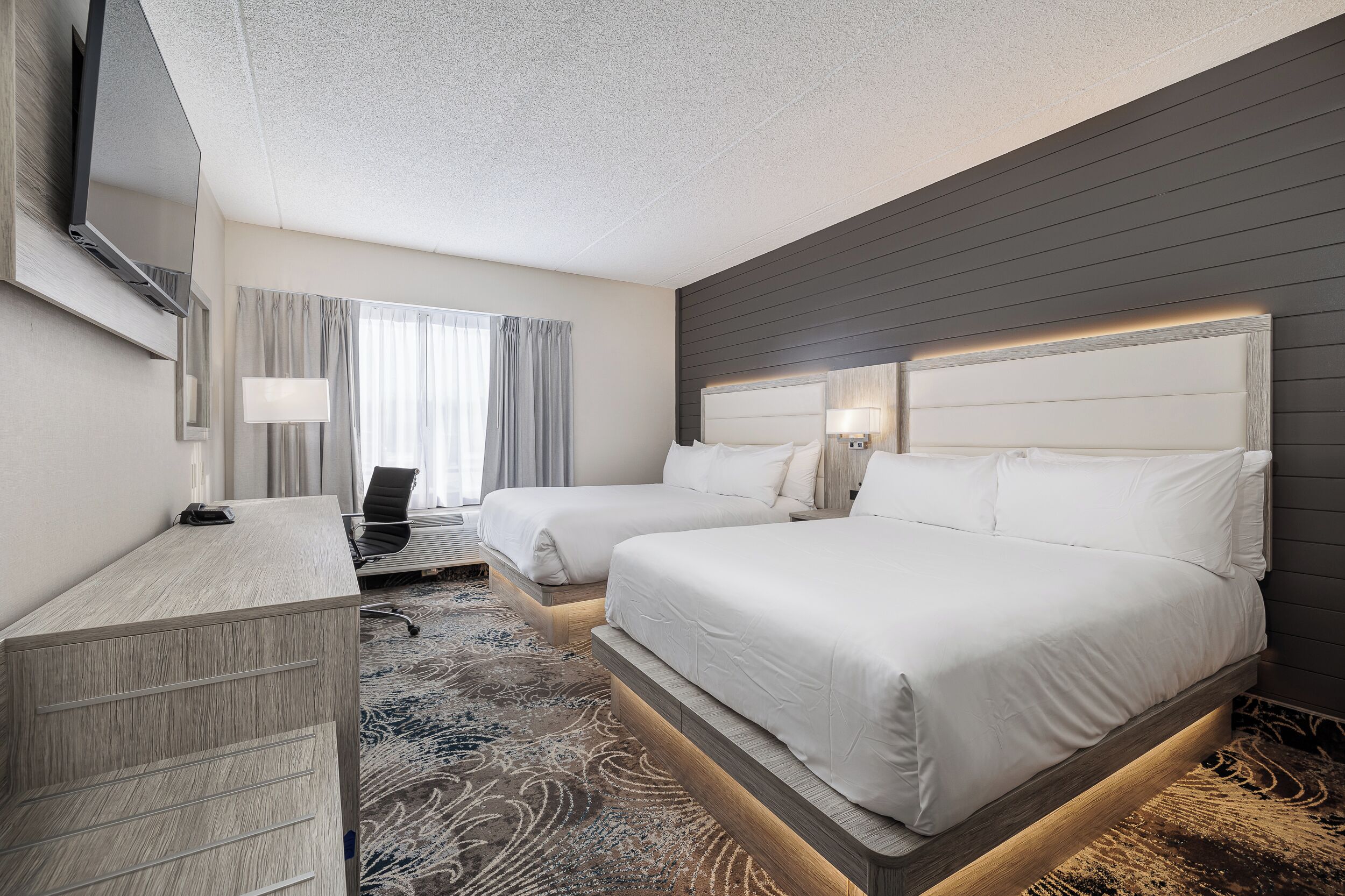 A hotel room with two beds, a desk, a chair, and a TV.