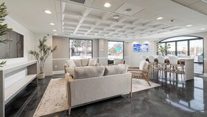 A modern hotel lobby with a sofa, chairs, a reception desk, and large windows offering views of the outside. - Oakfield Hotel & Suites, Ascend Collection, Rochester-Pittsford NY (Rochester)