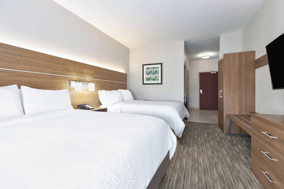 Une chambre d’hôtel avec deux lits, un bureau, une chaise, une télévision et un tableau encadré au mur.
