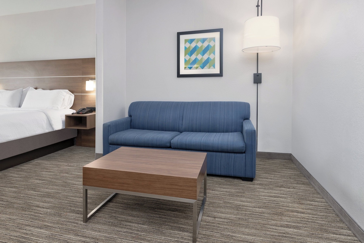 Une chambre d’hôtel avec un lit, un canapé bleu, une table basse en bois, une œuvre d’art encadrée et un lampadaire.