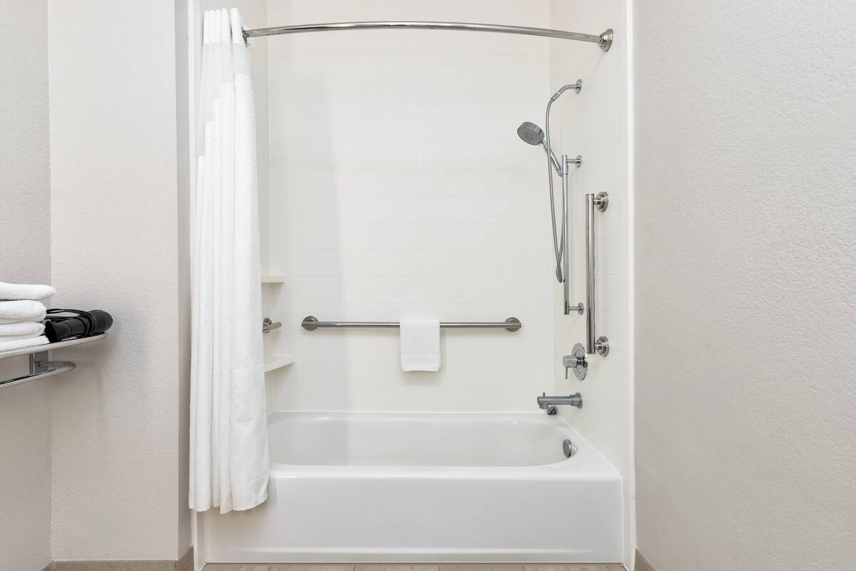 A modern bathroom with a white bathtub, a shower with a handheld showerhead, and a towel rack with a towel.