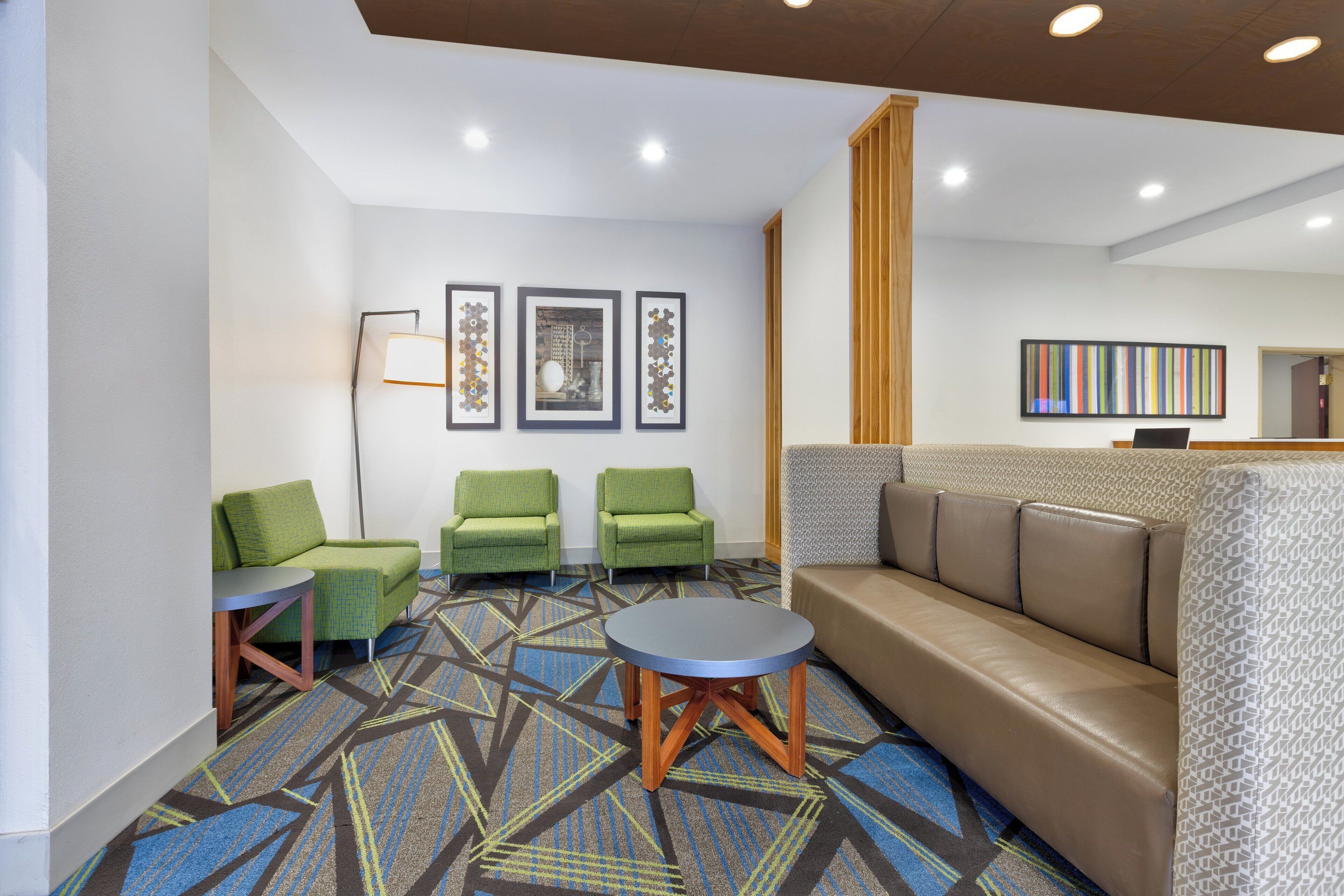 A modern lobby with a sofa, green chairs, a round table, and framed artwork on the walls.
