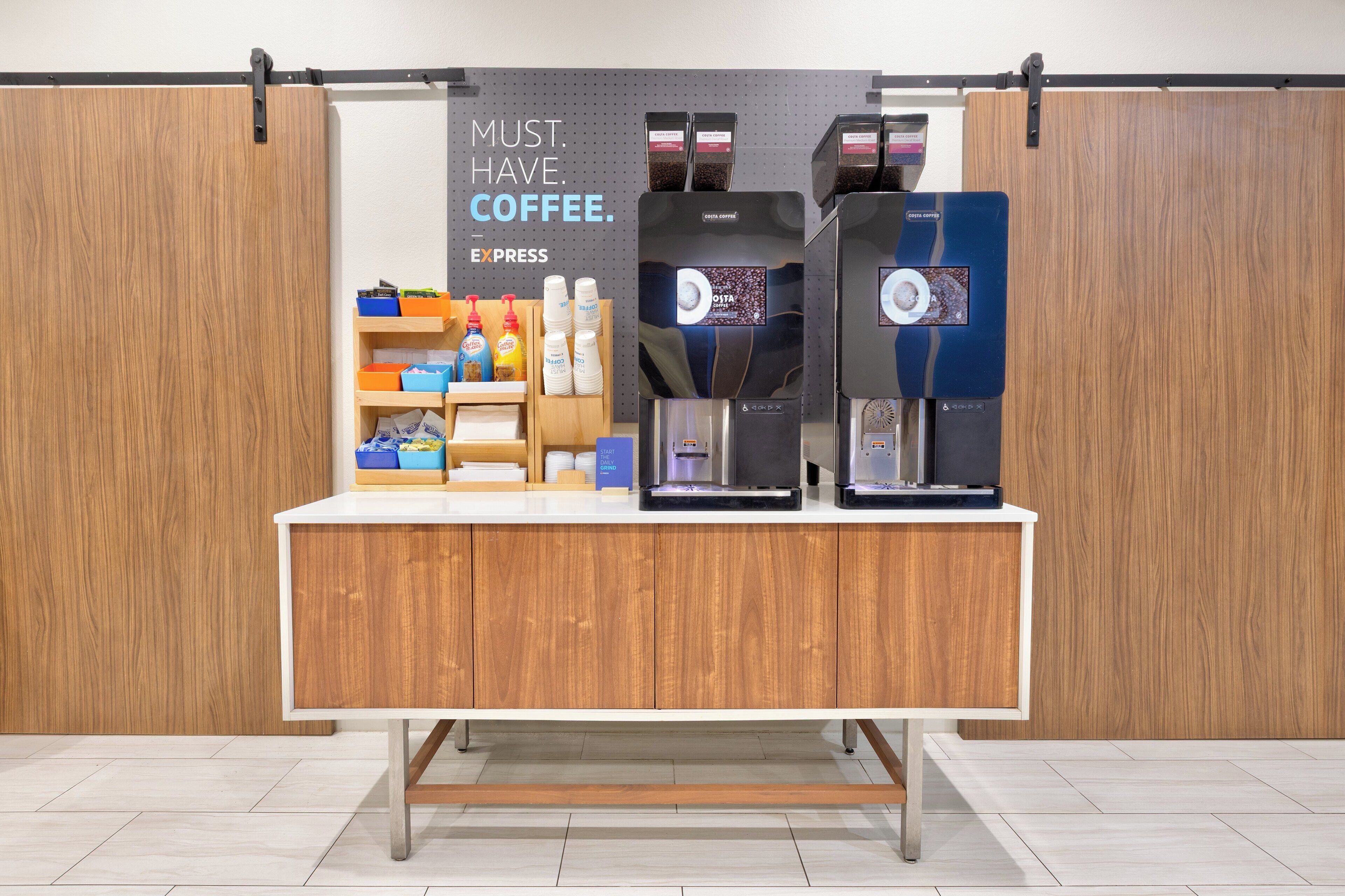 A coffee station with a sign that reads "MUST HAVE COFFEE." It includes a coffee machine, a water dispenser, and various coffee-related items.