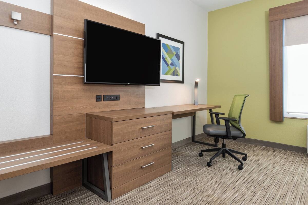 A modern office space with a wooden desk, a flat-screen TV, a green chair, and a framed abstract art piece on the wall.