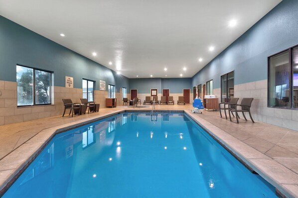 Une piscine intérieure à l’eau d’un bleu limpide, entourée de murs recouverts de carreaux beiges et surmontée d’un plafond bleu.