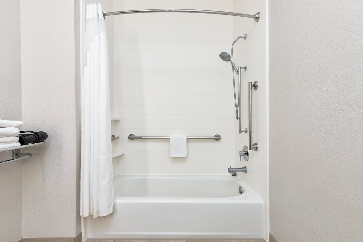 Une salle de bain moderne avec une baignoire blanche, une douche équipée d’un pommeau de douche à main et un porte-serviettes avec une serviette.