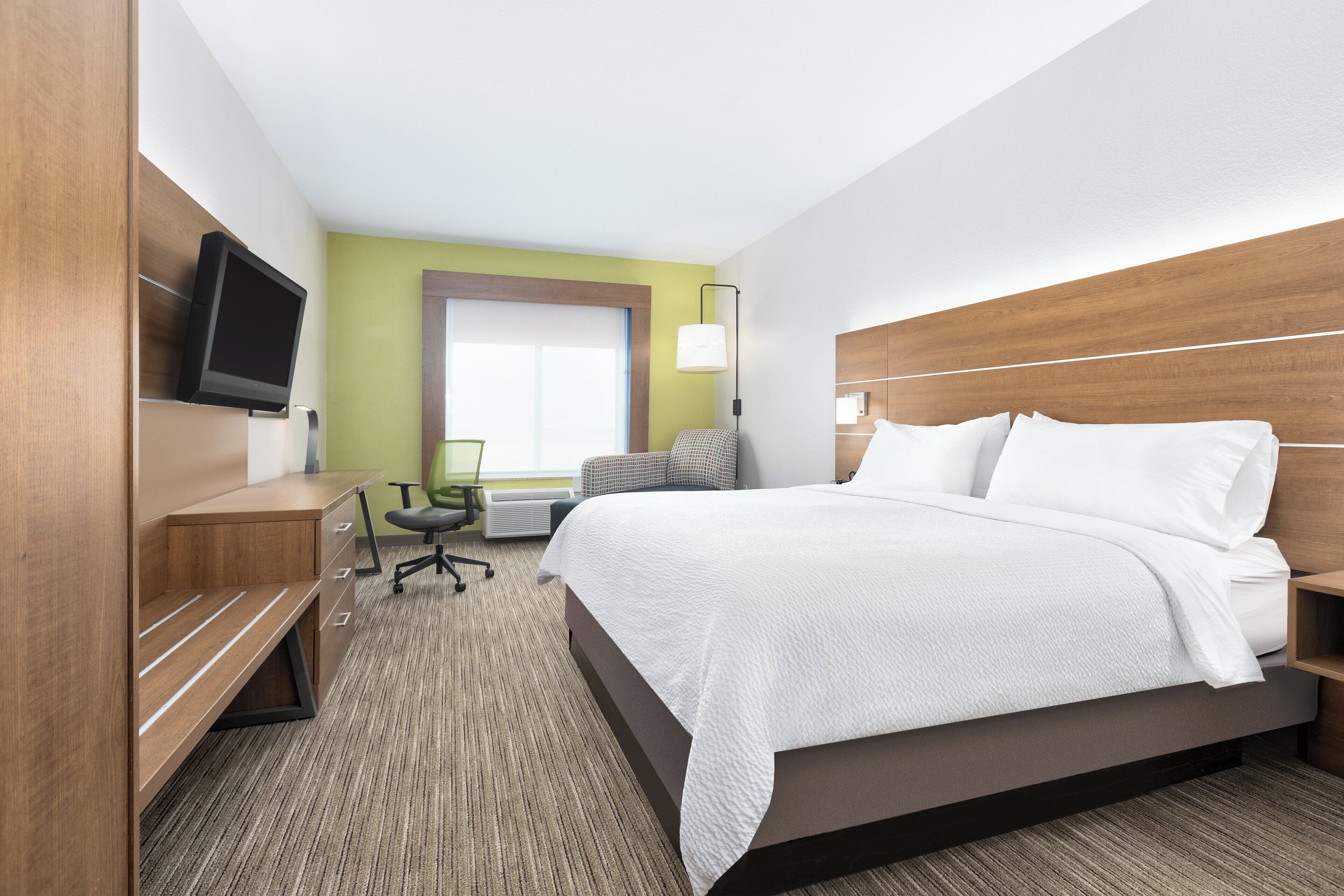 A hotel room with a large bed, a desk with a chair, a television, and a window with blinds.