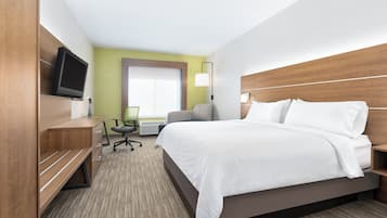 A hotel room with a large bed, a desk with a chair, a television, and a window with blinds.