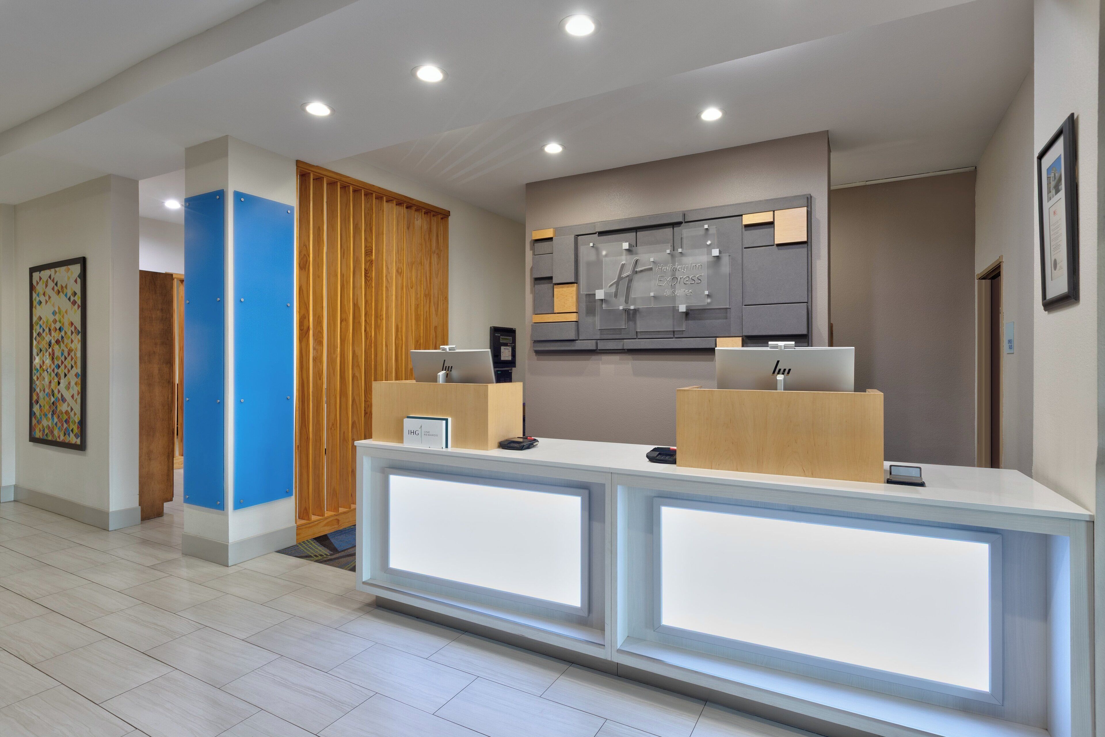 A modern reception desk with a digital display, a wooden panel wall, and a framed artwork above it.