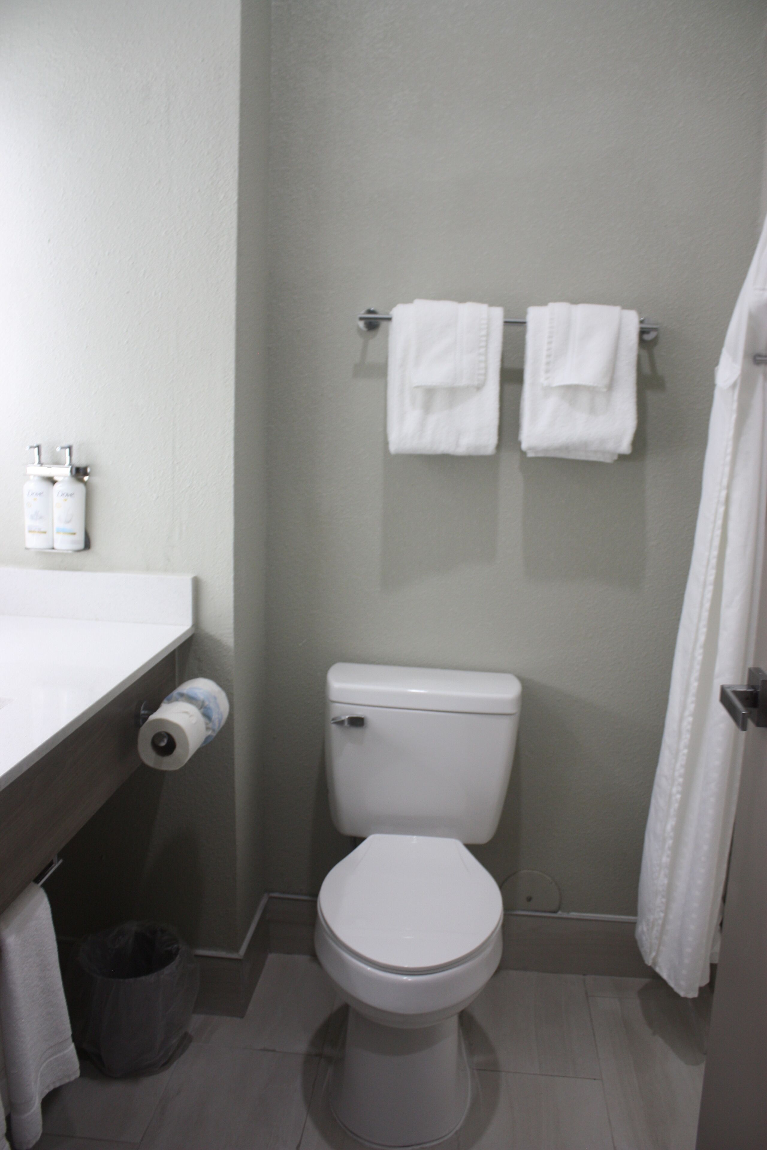 Un baño pequeño con inodoro, toallero con dos toallas, dispensador de papel higiénico y un cesto de basura.