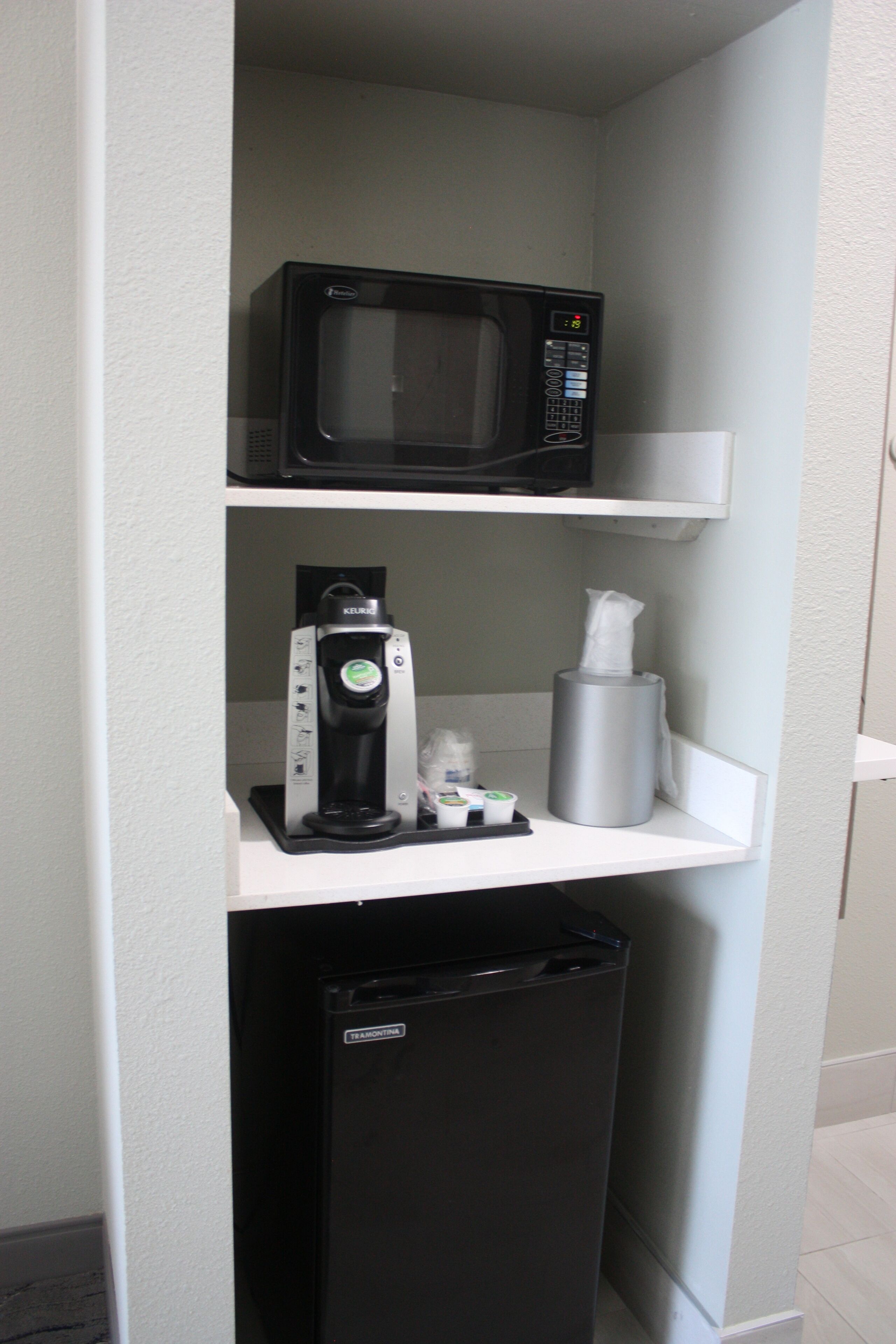 Een kitchenette met een magnetron, koffiezetapparaat en koelkast.