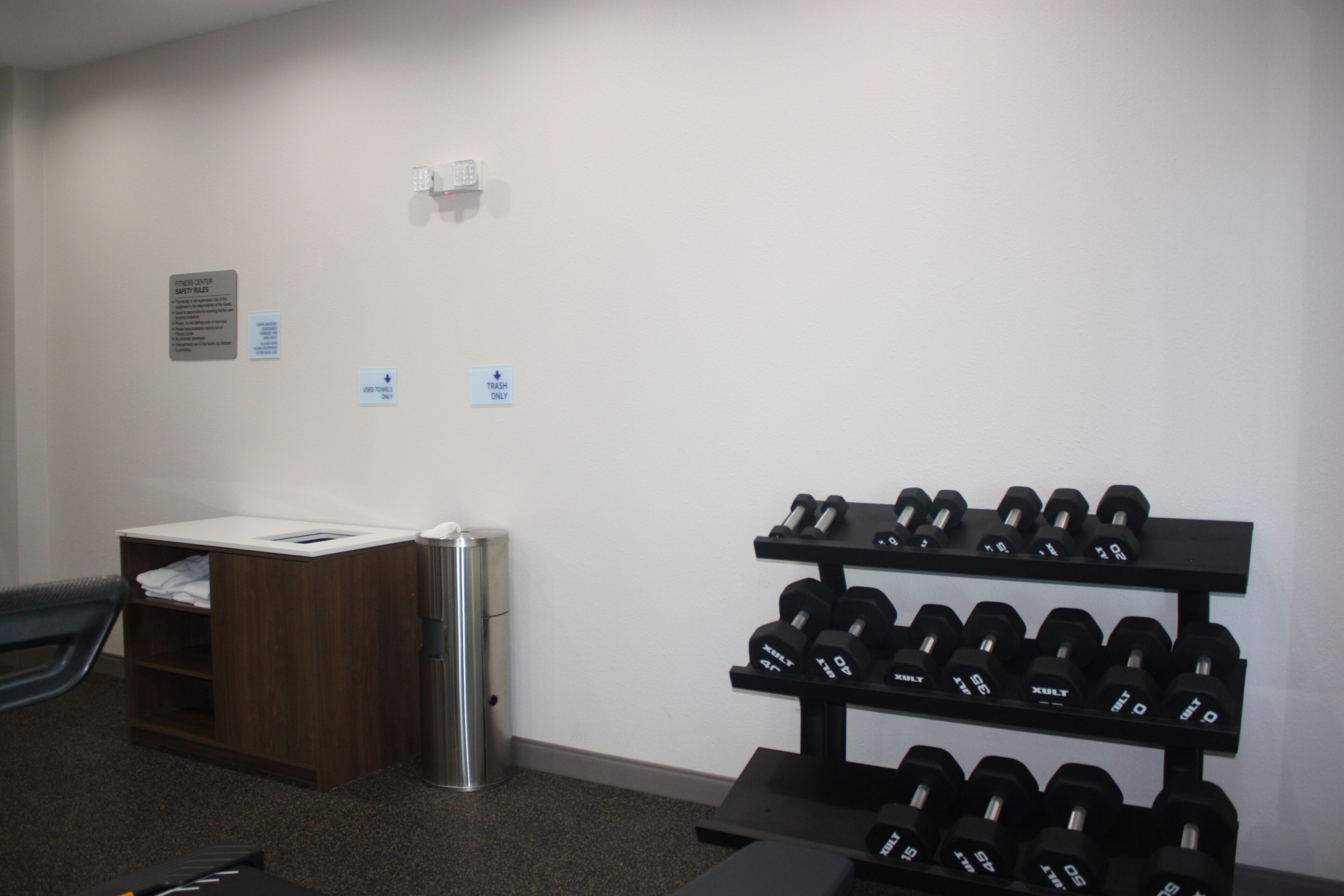 A gym with a dumbbell rack, a trash bin, and a small desk with a chair.