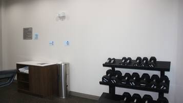 A gym with a dumbbell rack, a trash bin, and a small desk with a chair.