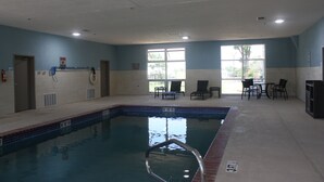 Una piscina interior con borde de azulejos, una silla de salvavidas y una zona de estar con sillas y una mesa.