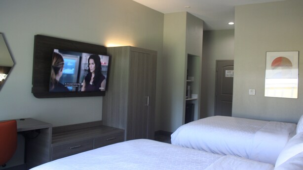Una habitación de hotel con dos camas, un televisor montado en la pared, un armario y un pequeño escritorio con una silla.