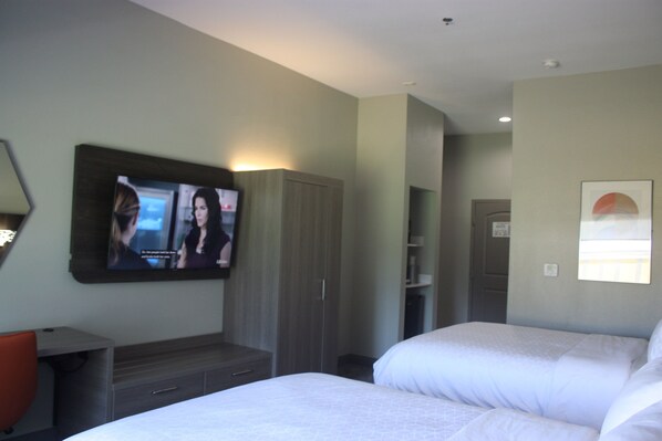 A hotel room with two beds, a TV mounted on the wall, a wardrobe, and a small desk with a chair. - Holiday Inn Express Hotel & Suites Shamrock North by IHG (Shamrock)