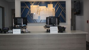 Mostrador de recepción de Holiday Inn Express con dos estaciones de ordenador, un diseño mural grande en azul y dorado, y un cartel que indica la ubicación.