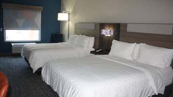 Habitación de hotel con dos camas, una mesita de noche, una lámpara y una ventana con persianas.
