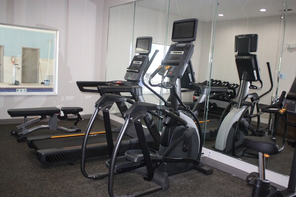 A gym with treadmills, ellipticals, and a mirrored wall.