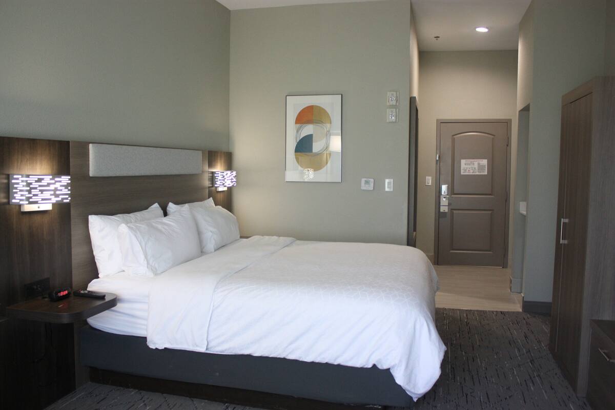 A hotel room with a bed, bedside table, wall art, and a door.
