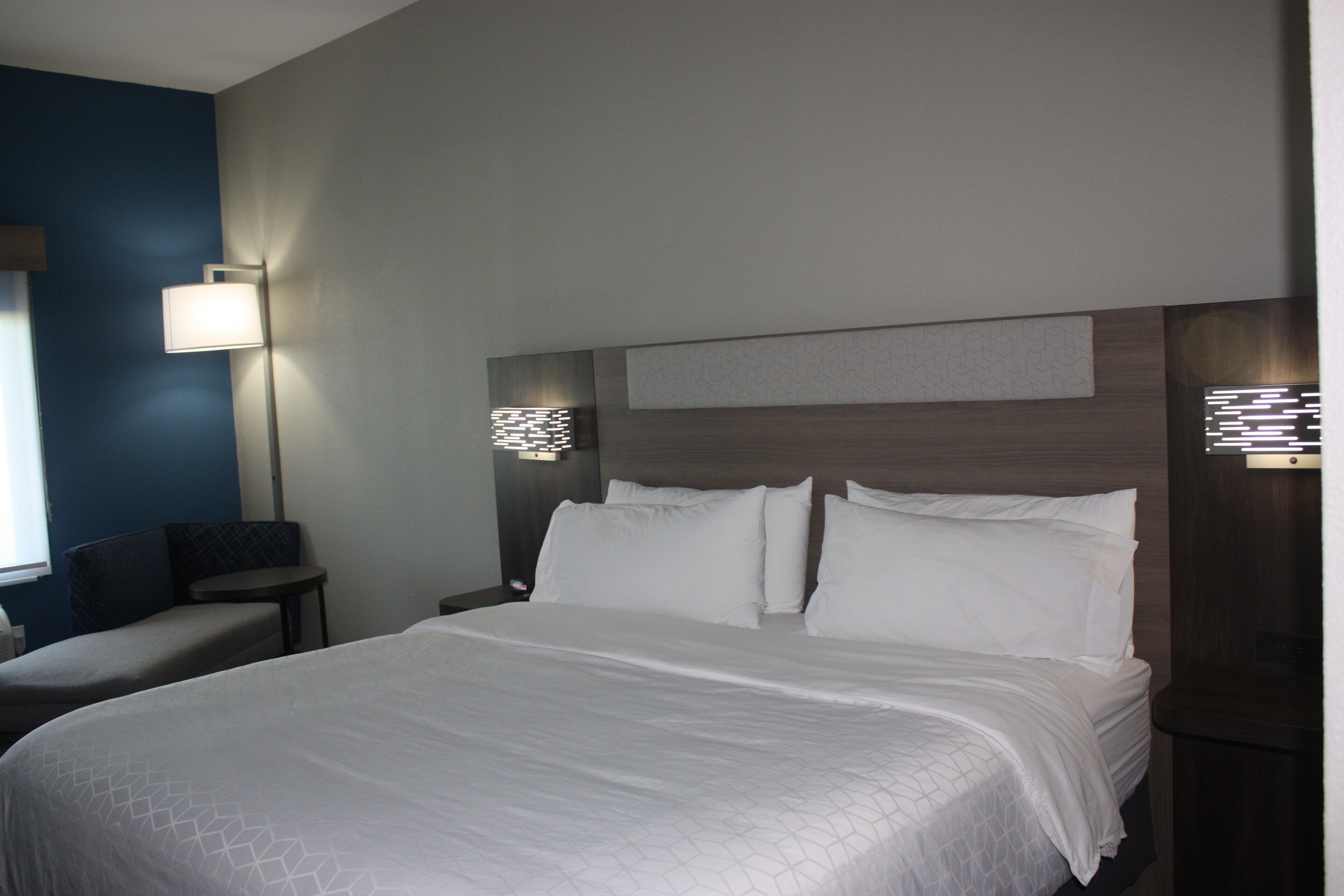 A hotel room with a large bed, two bedside tables, a nightstand, and a wall-mounted lamp.