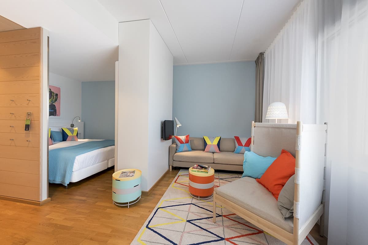 A modern hotel room with a bed, sofa, and a small table.