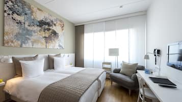 Quarto de hotel com uma cama grande, uma escrivaninha com cadeira, uma luminária e um quadro na parede.