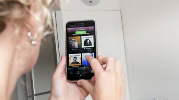 Una persona sosteniendo un teléfono inteligente que muestra una aplicación de música con varios artistas y canciones.