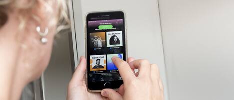 A person holding a smartphone displaying a music app with various artists and songs.