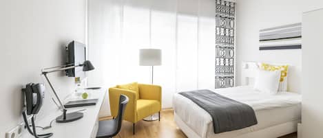 Une chambre d’hôtel moderne équipée d’un bureau, d’une chaise, d’un lit et d’une grande fenêtre avec des rideaux.